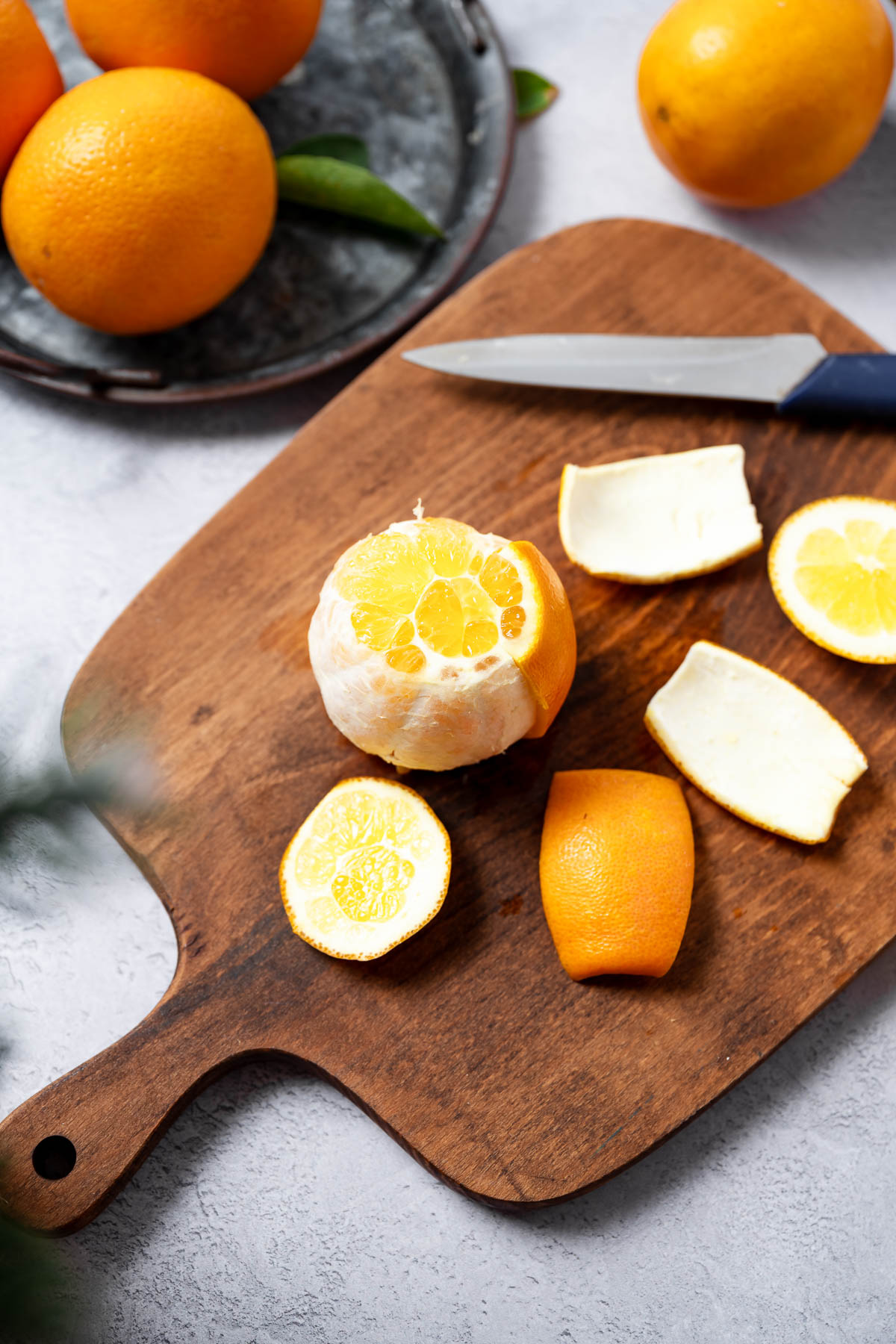 A partially peeled orange on a wooden cutting board