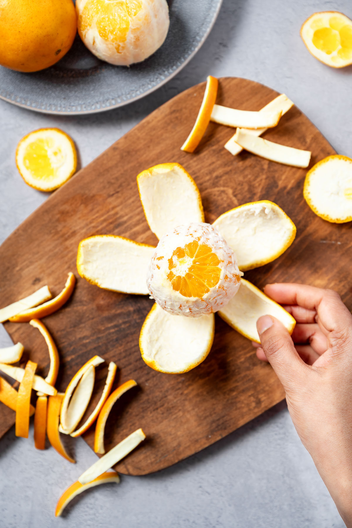 A person peeling an orange on a wooden board with strips of orange peel scattered around