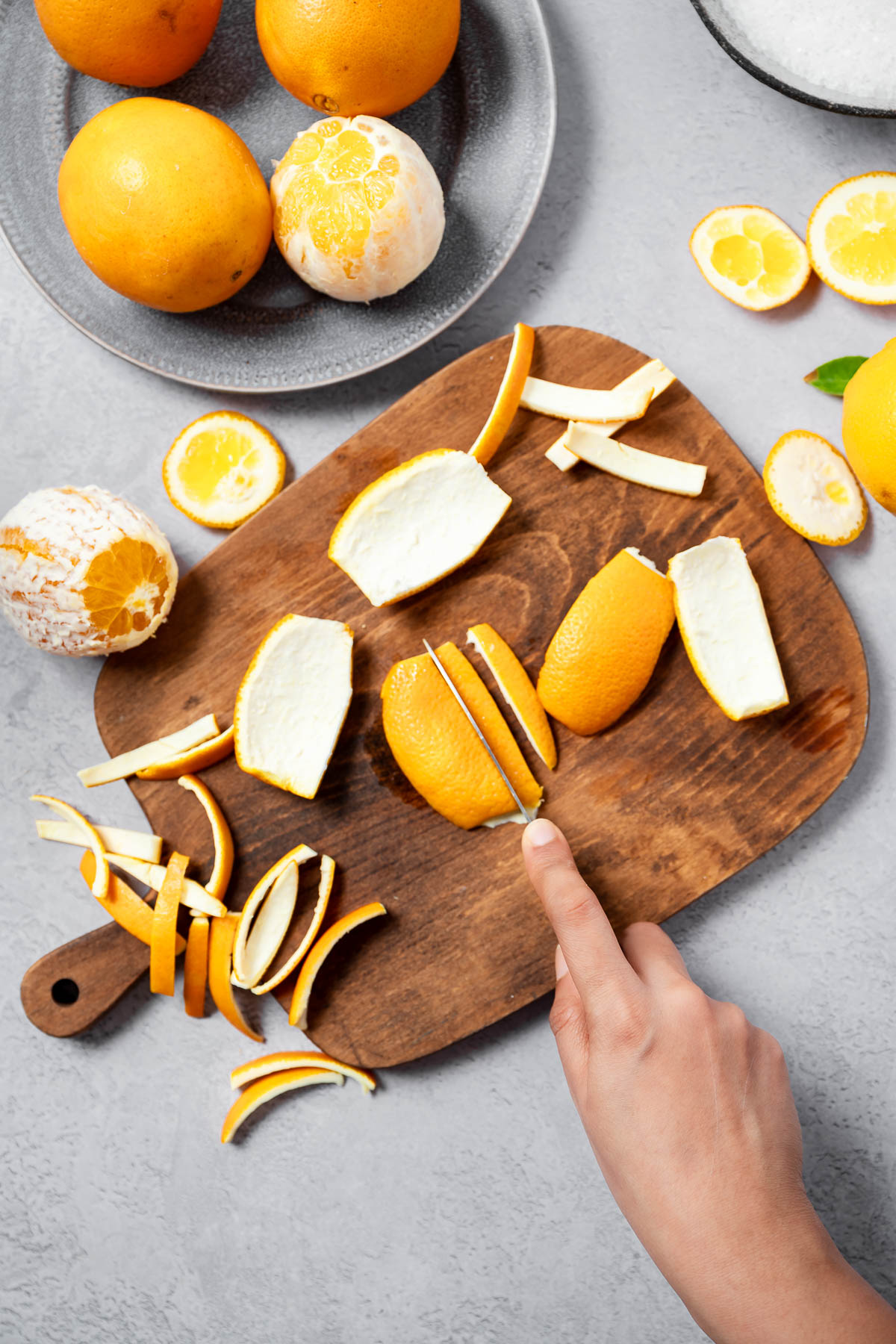 A person using a knife to slice an orange peel into long strips