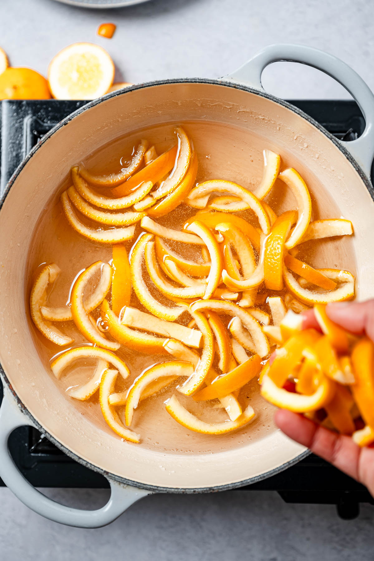 Orange peels being added to a pot of sugary syrup
