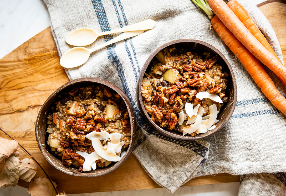 2 coconut bowls of healthy carrot cake oatmeal topped with candied pecans, coconut flakes and shredded carrots.