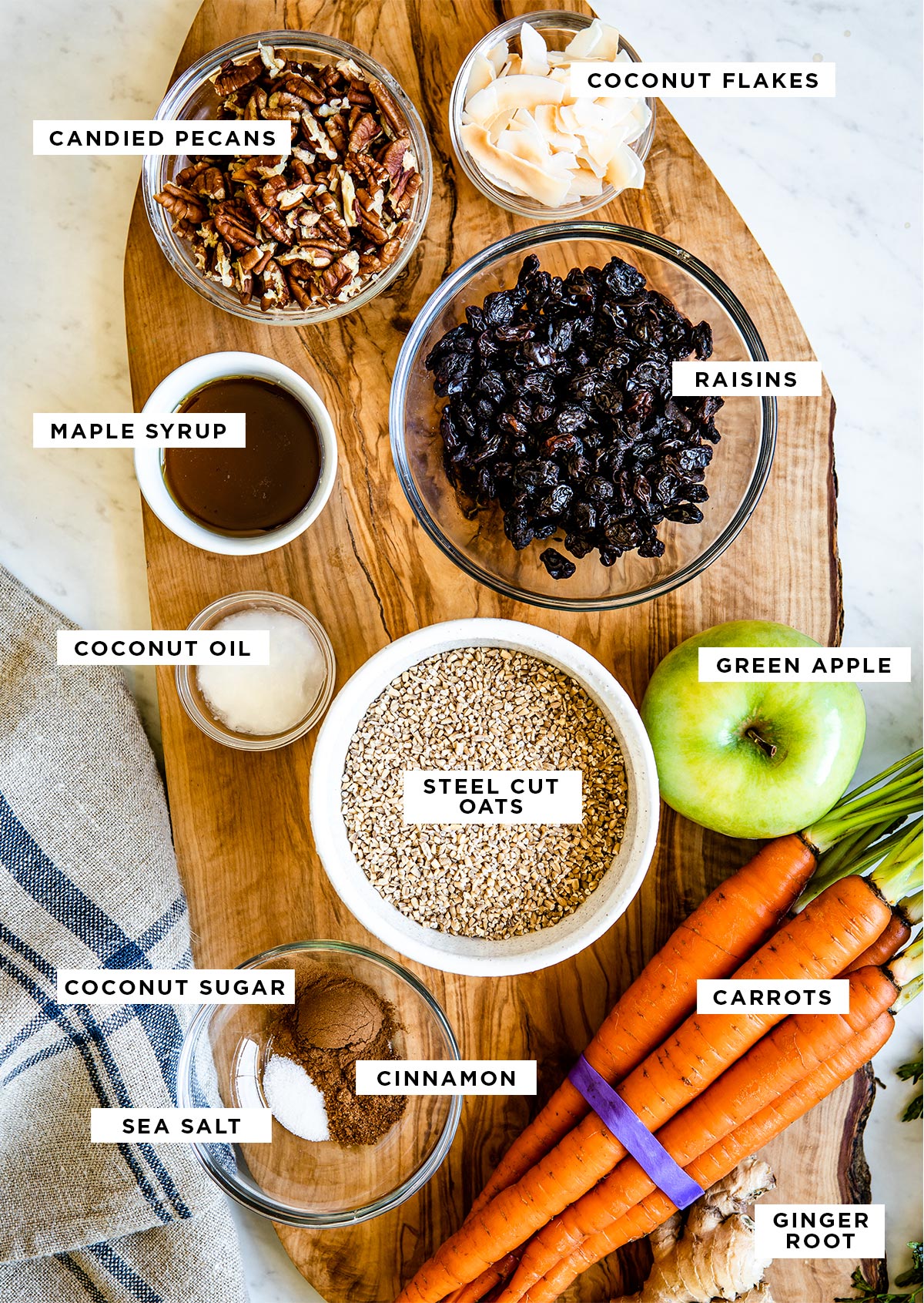 ingredients for stovetop oatmeal labeled: coconut flakes, candied pecans, maple syrup, raisins, coconut oil, steel cut oats, green apple, carrots, coconut sugar, sea salt, cinnamon and ginger root.