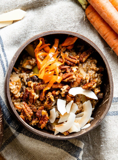 coconut bowl full of carrot cake oatmeal topped with candied pecans, coconut flakes and shredded carrots.