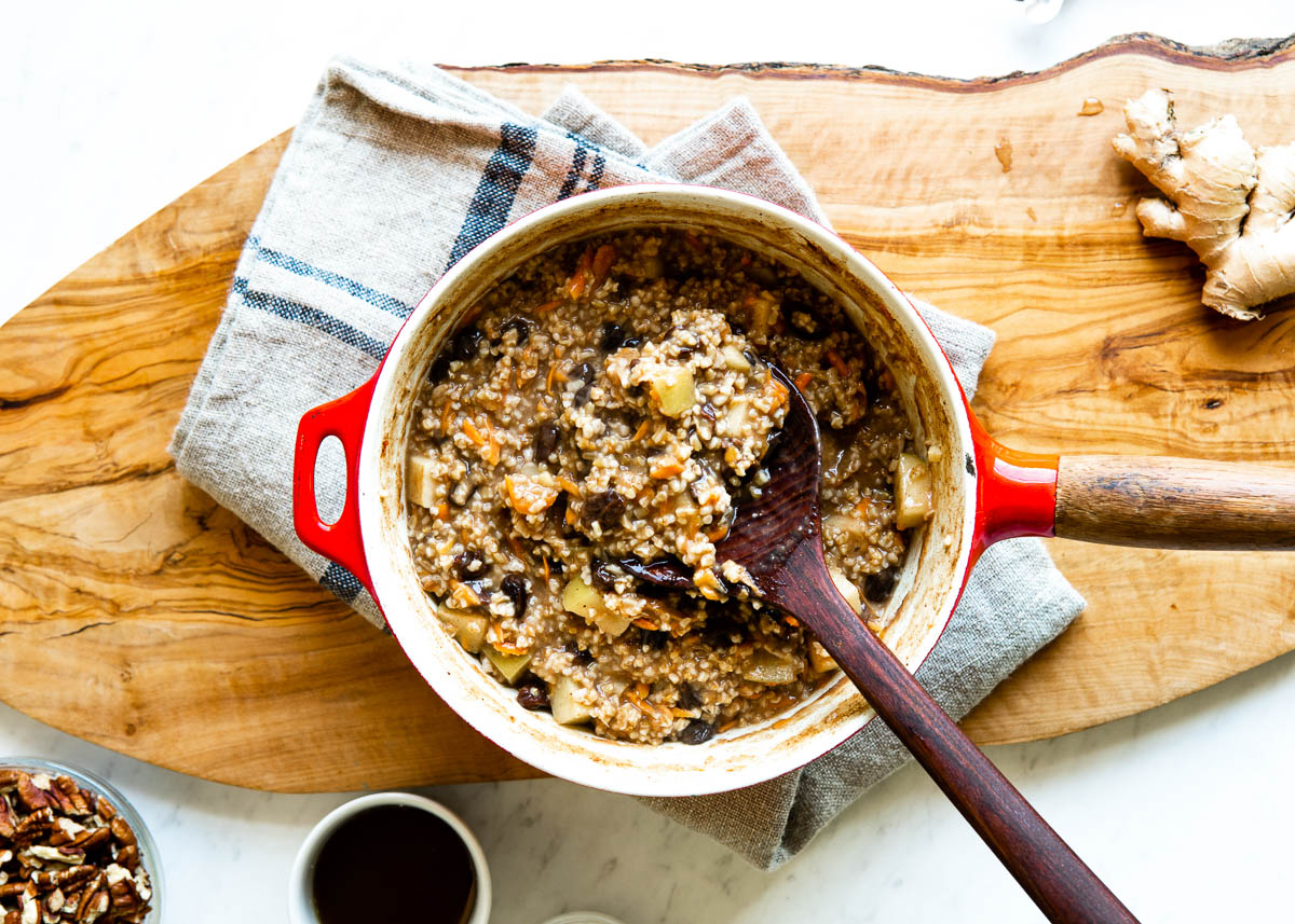 almost cooked oatmeal with raisins, apples and carrots getting stirred with a dark wooden spoon.