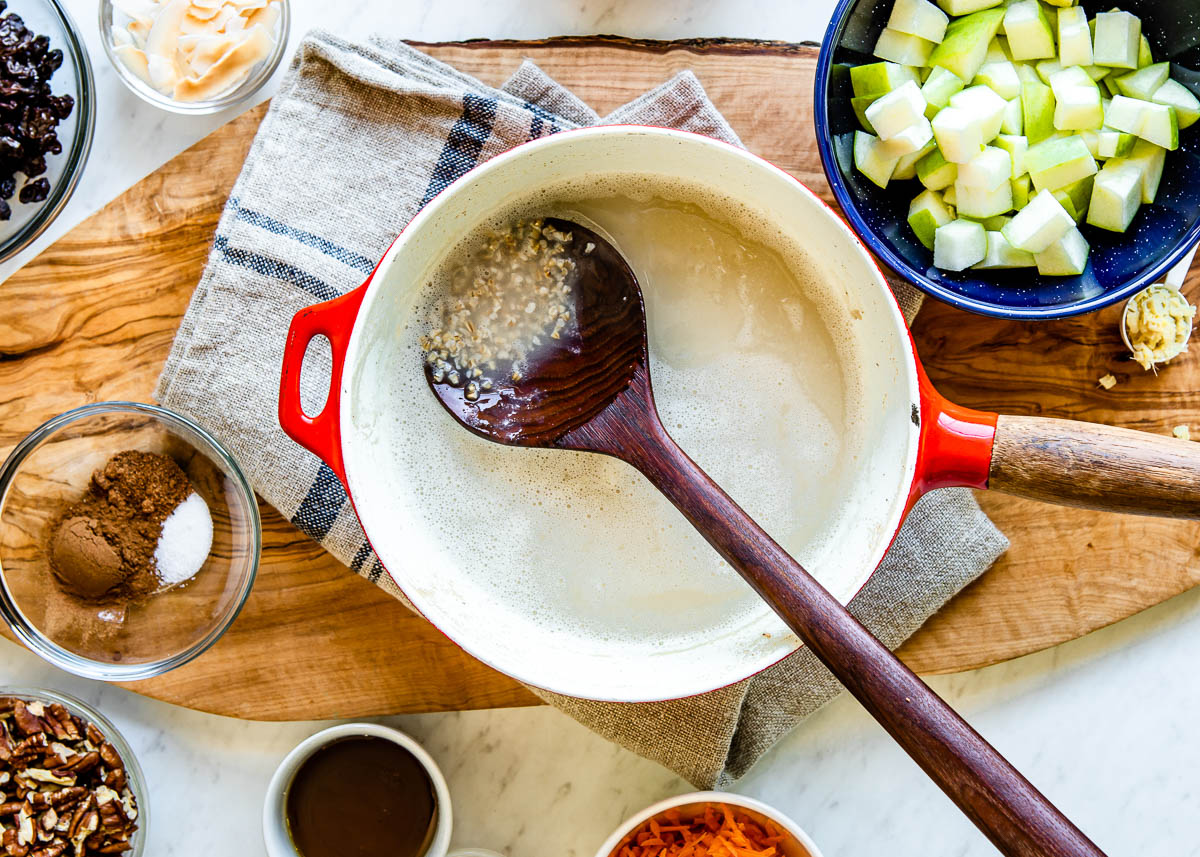 dark wooden spoon stirring steel cut oats and water together in a red sauce pan with a wooden handle.