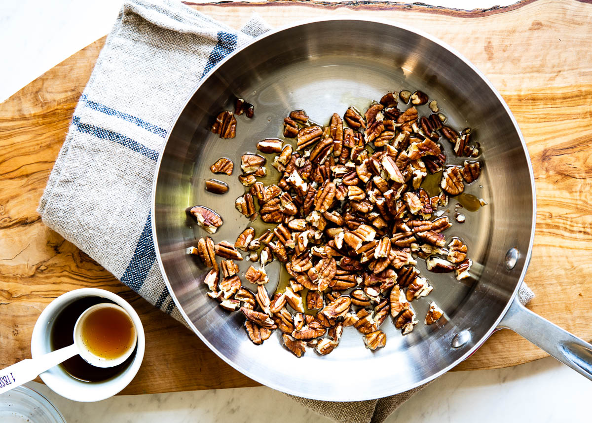 stainless steel skillet with chopped pecans in maple syrup.