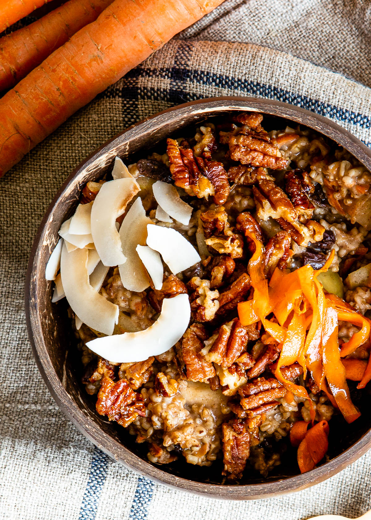 coconut bowl full of healthy carrot cake oatmeal topped with candied pecans, coconut flakes and shredded carrots.