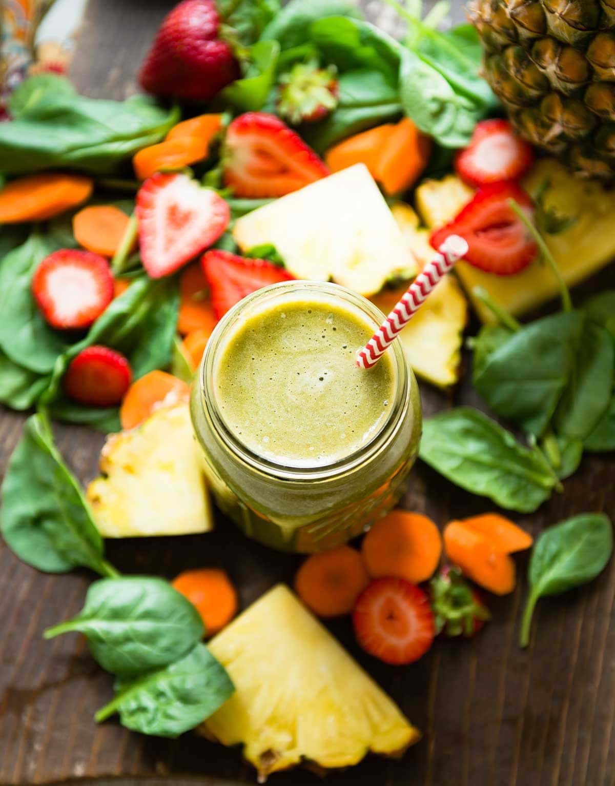 green smoothie in a glass jar with a paper straw, surrounded by fresh ingredients.