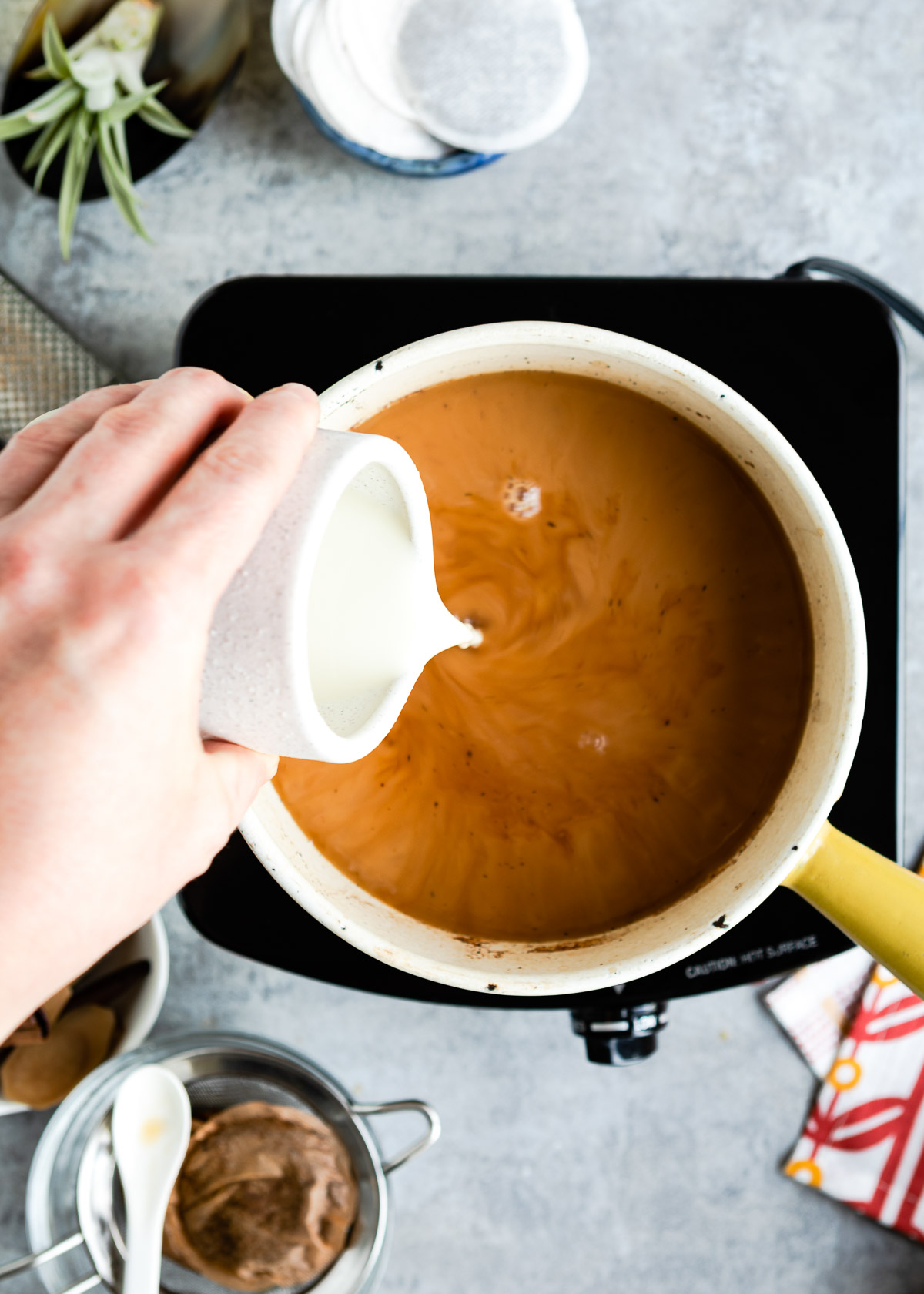 A person adding oat milk into the tea mix