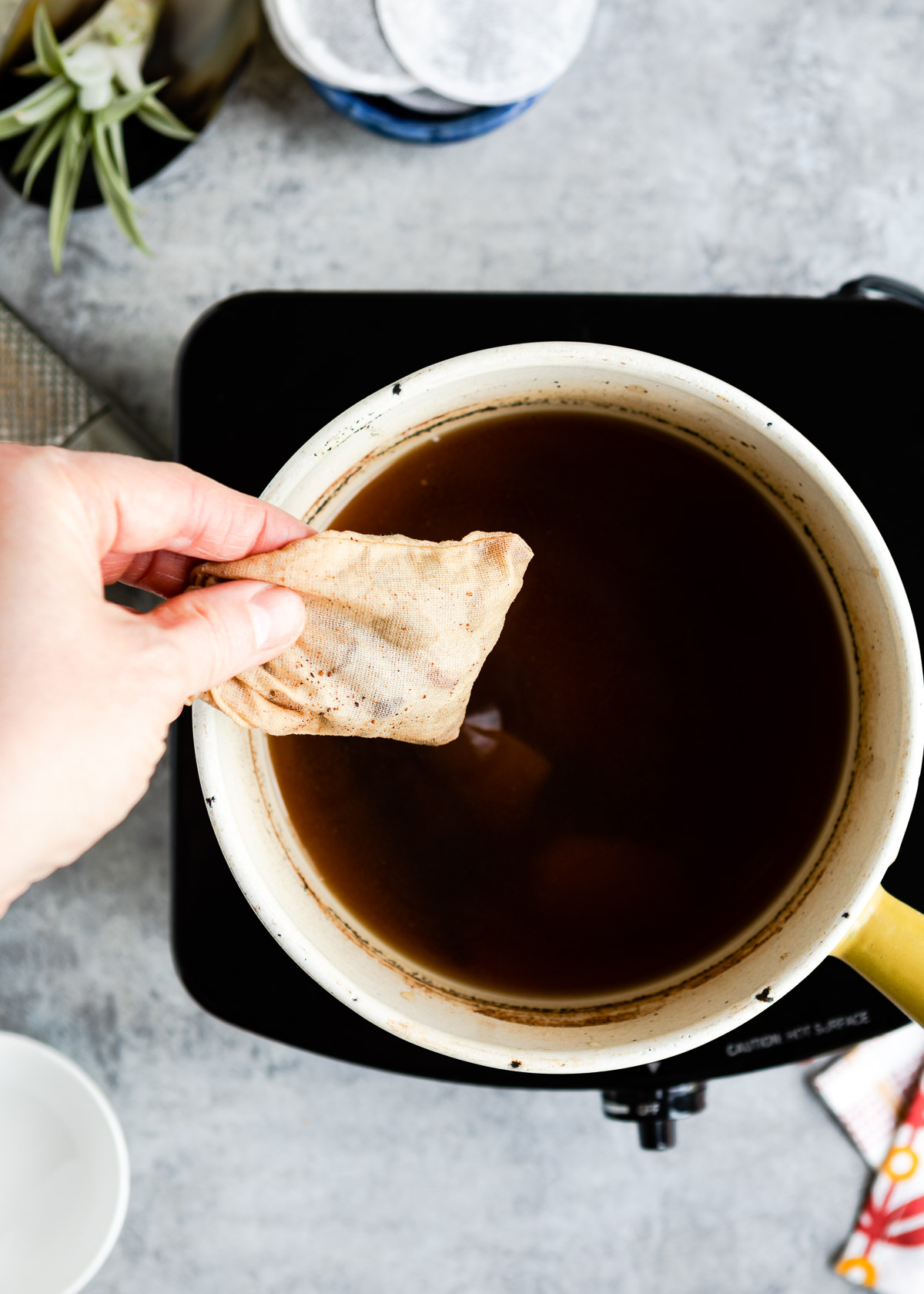 Person removing a spice bag from a saucepan of brewed chai tea base