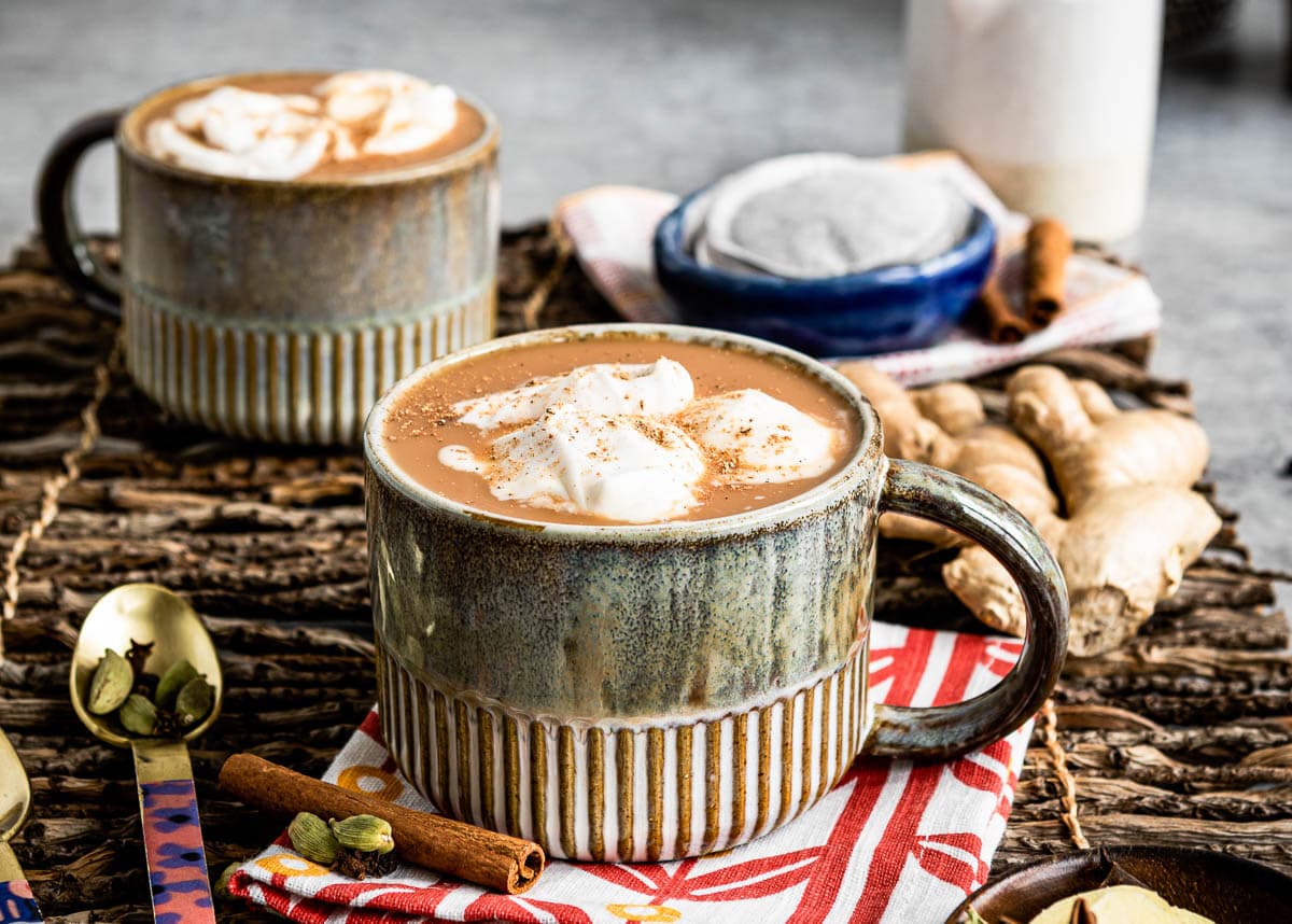2 mugs of homemade chai tea latte topped with coconut whipped cream.
