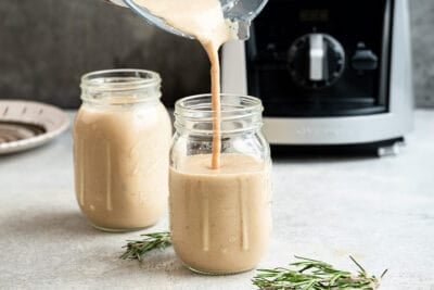 Creamy smoothie being poured into glass jars from blender for a healthy drink.
