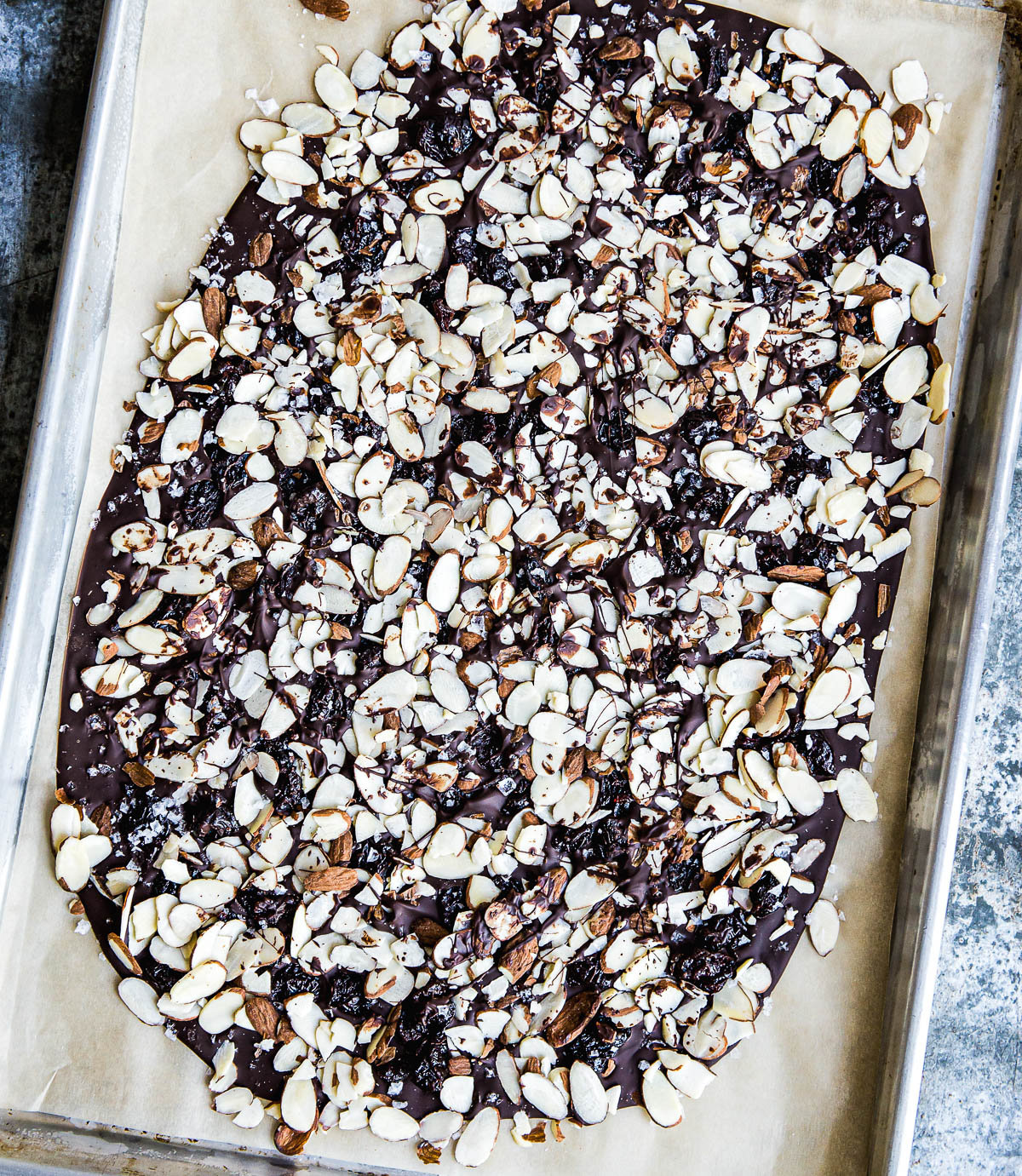 melted chocolate spread out on a parchment lined baking sheet, topped with sliced almonds.