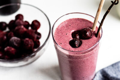 Cherry vanilla smoothie in a glass with vanilla bean on top.