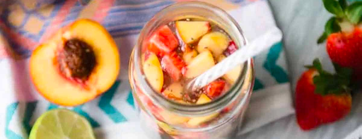 drink in a mason jar with chopped strawberries and peaches on top with a straw