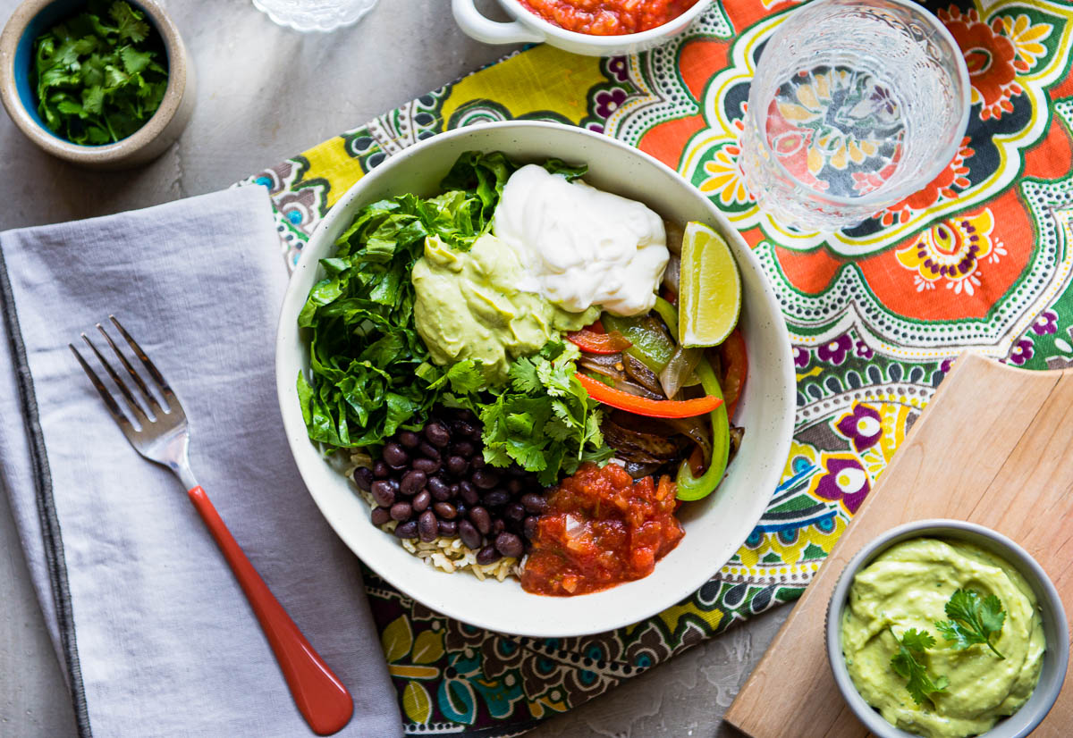 loaded burrito bowl topped with cashew cream, limes, avocado crema, cilantro, beans and salsa.