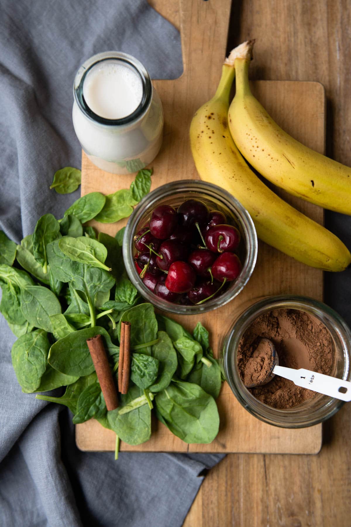 ingredients for a dessert smoothie including almond milk, bananas, cherries, spinach, cacao and cinnamon.