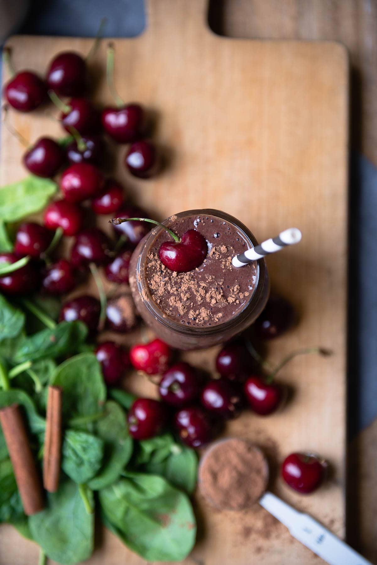 chocolate smoothie with paper straw and topped with cacao and a fresh cherry.