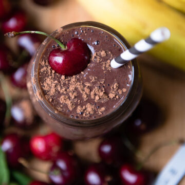 overhead photo of a chocolate cherry smoothie topped with cacao powder and a red cherry + a paper straw