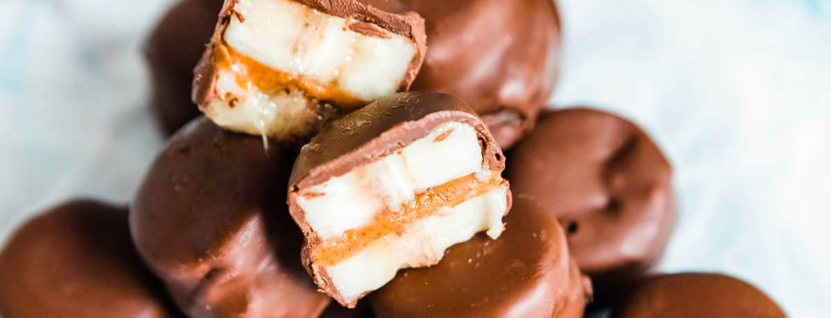 chocolate covered banana bites stacked on a plate with one of them cut in half showing the cross section