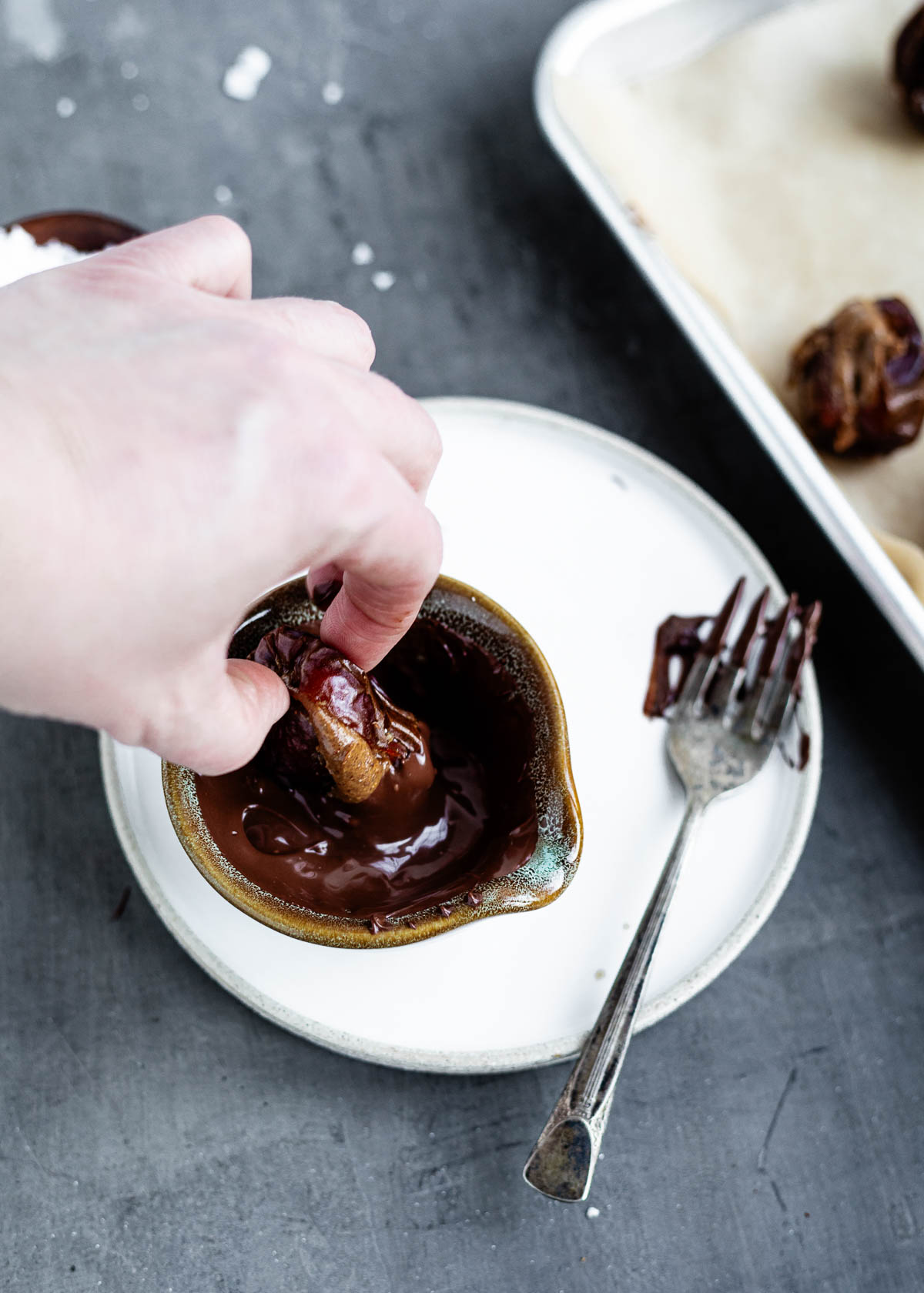 A hand dipping a stuffed date into melted chocolate.