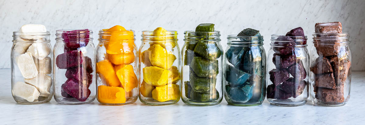 A long row of Mason jars displaying a vibrant rainbow of various smoothie cubes.
