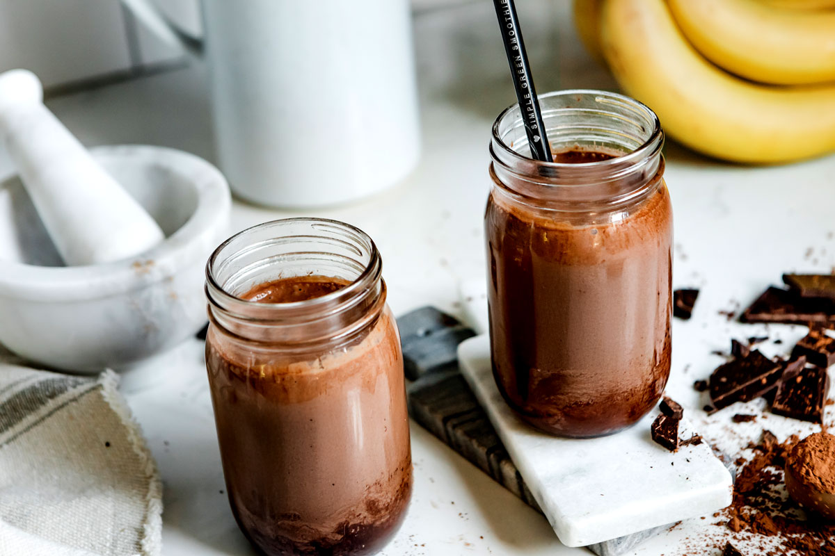 Two mason jars filled with chocolate peanut butter smoothie with cacao powder and chocolate bars.