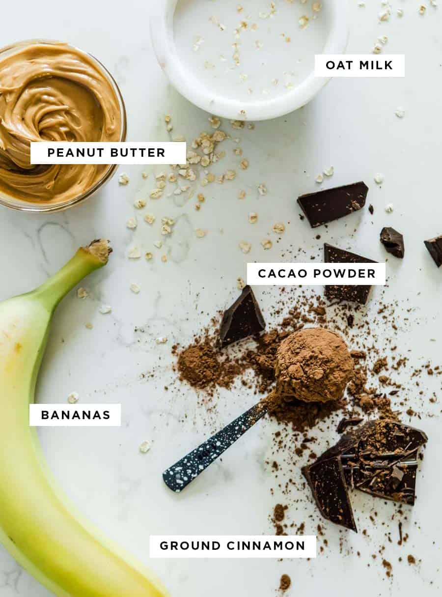 ingredients for a chocolate protein shake including oat milk, peanut butter, cacao powder, banana and ground cinnamon.