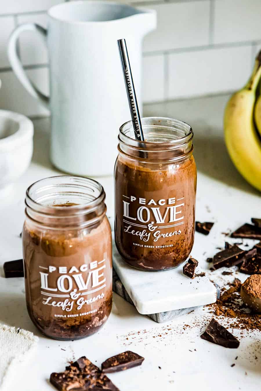 2 jars of chocolate peanut butter smoothie with straws. Jars have white writing that says Peace, Love & Leafy Greens Simple Green Smoothies.