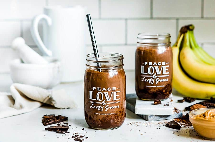 2 jars of smoothie on a counter surrounded by chocolate, banana and peanut butter.