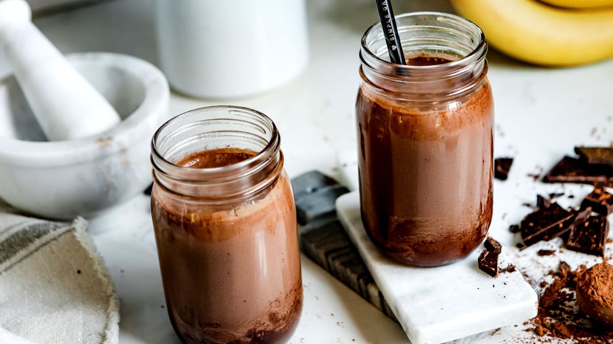 Two mason jars filled with chocolate peanut butter smoothie with cacao powder and chocolate bars.