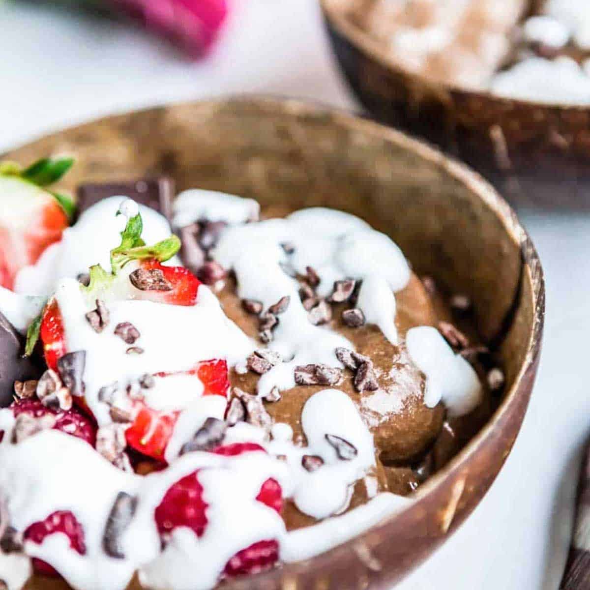 chocolate smoothie in brown bowl topped with strawberry, cacao and whipped coconut milk.
