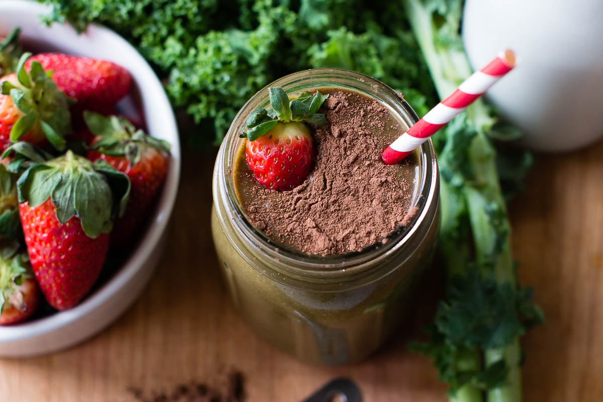 Chocolate strawberry smoothie in a glass mason jar, topped with cacao powder and a fresh strawberry.