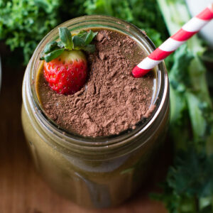 Chocolate strawberry smoothie in a glass mason jar, topped with cacao powder and a fresh strawberry.