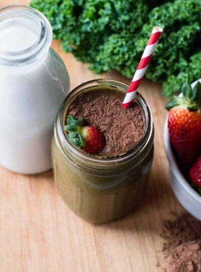 chocolate strawberry smoothie topped with cacao and fresh strawberries with a striped straw.