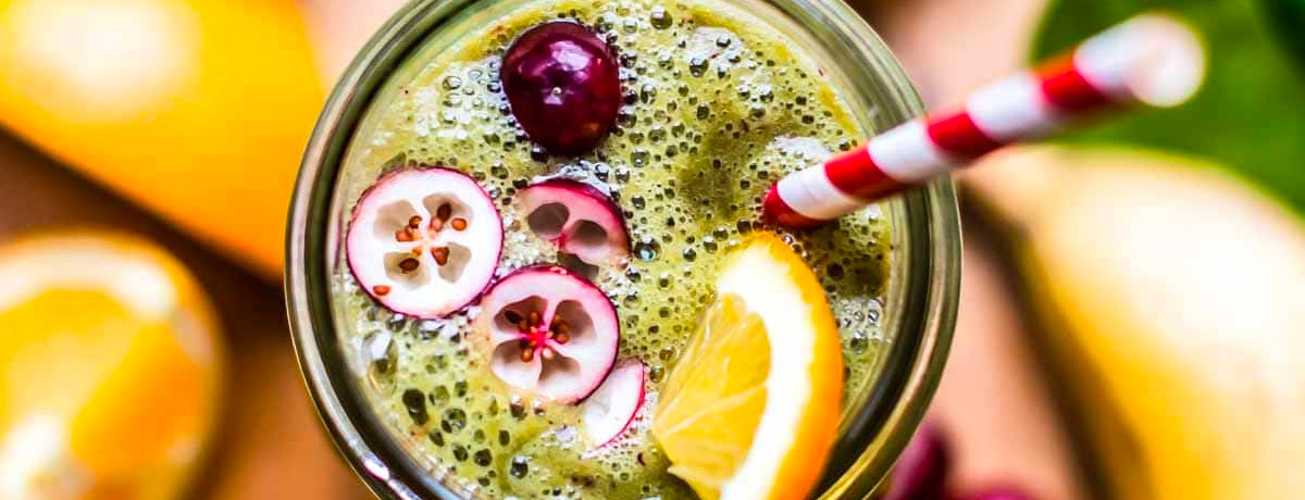 top down look at a green smoothie in a jar with fresh cut cranberries and oranges
