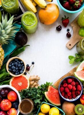 Colorful array of fresh fruits and green smoothies on a white background.