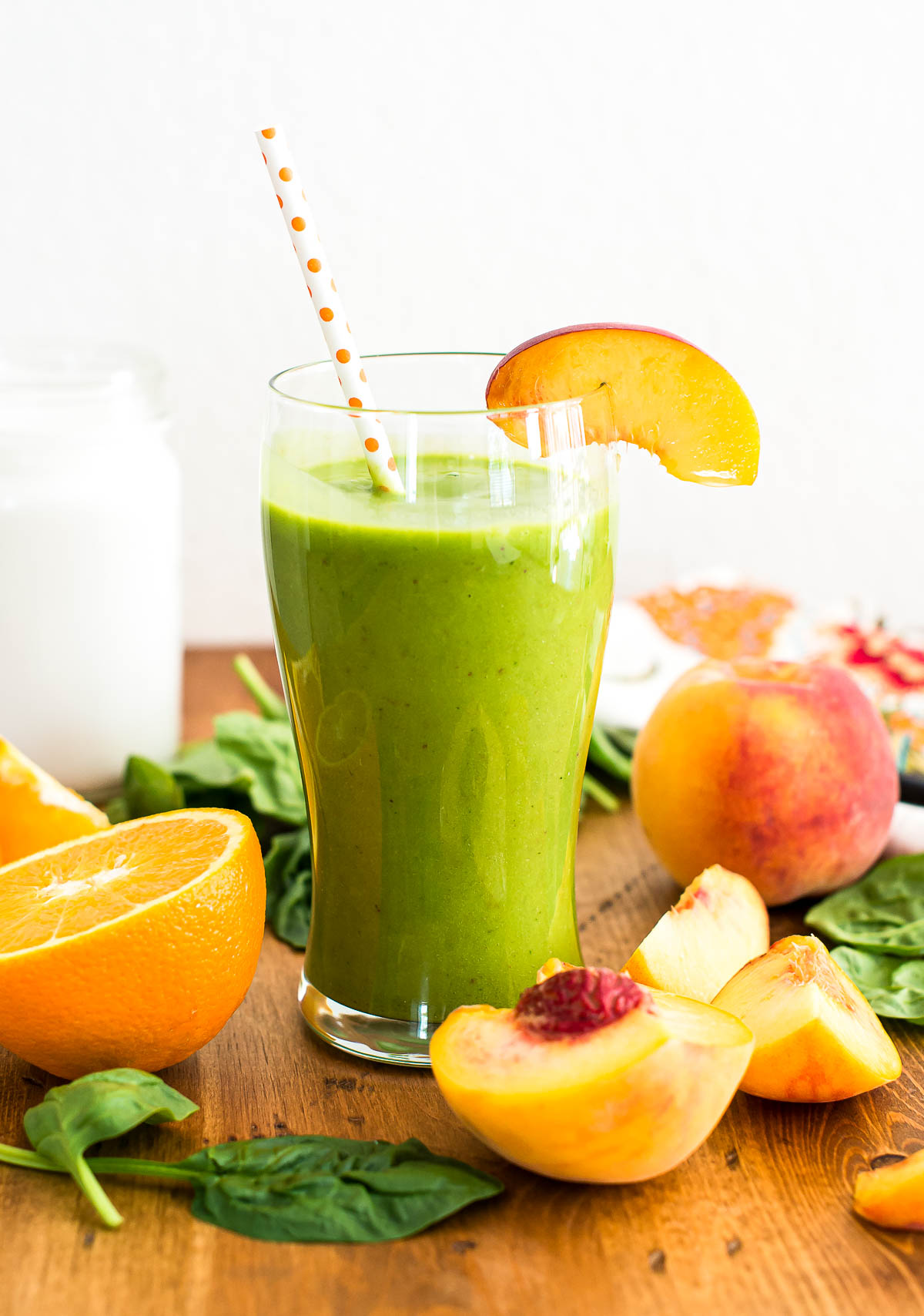 creamy green smoothie in glass with polka dot paper straw and a peach slice.