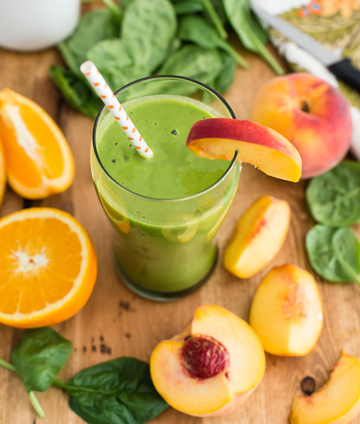 green smoothie with peaches and coconut milk in tall glass with paper straw.