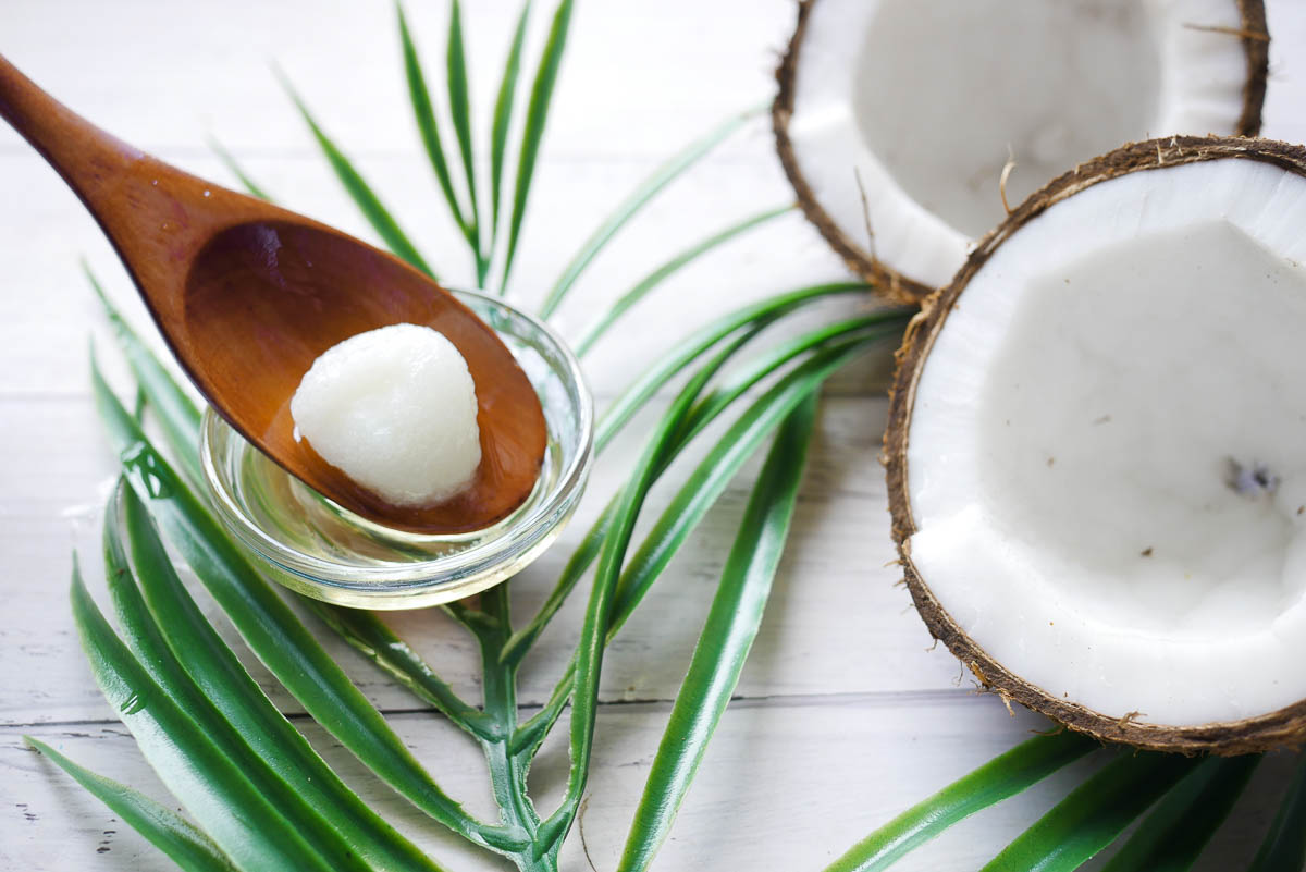 wooden spoon with solid coconut oil sitting in it next to 2 halves of fresh coconut.