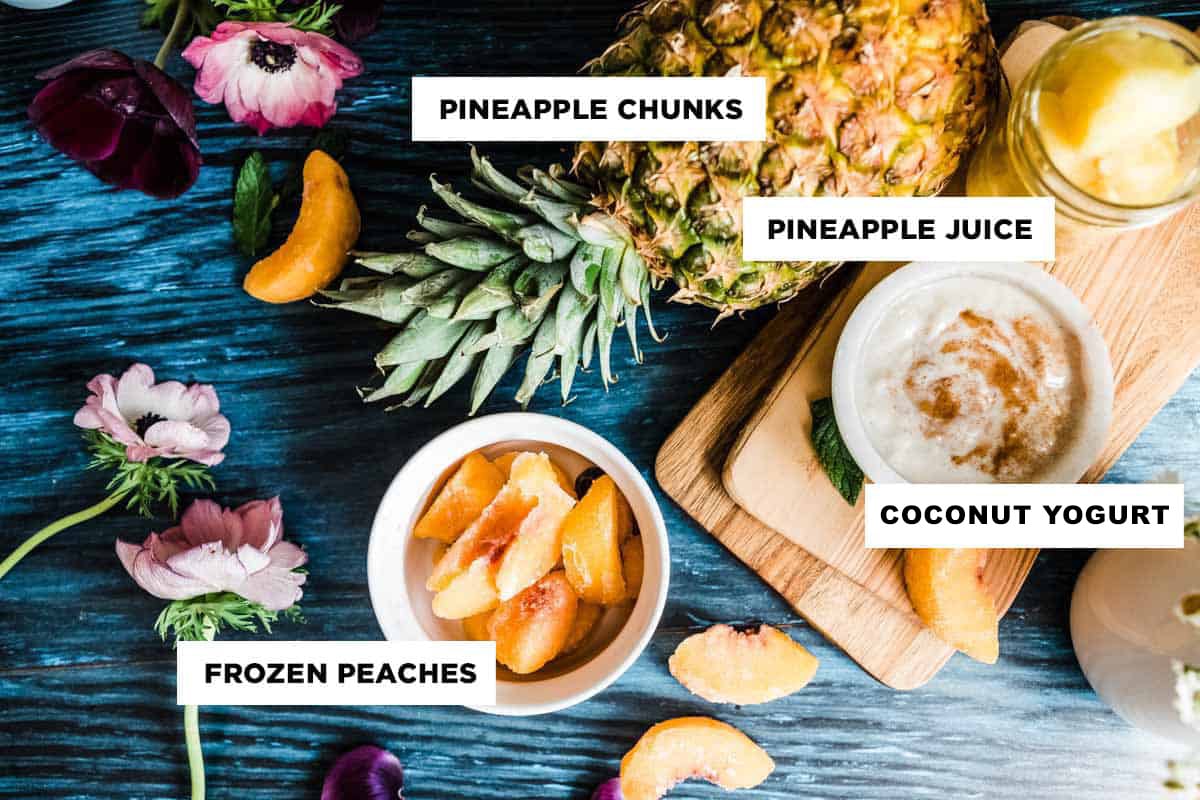 ingredients for a coconut pineapple smoothie, including pineapple chunks, pineapple juice, coconut yogurt, and frozen peaches.