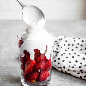 dairy-free coconut whipped cream getting scooped over fresh strawberries in a clear glass.