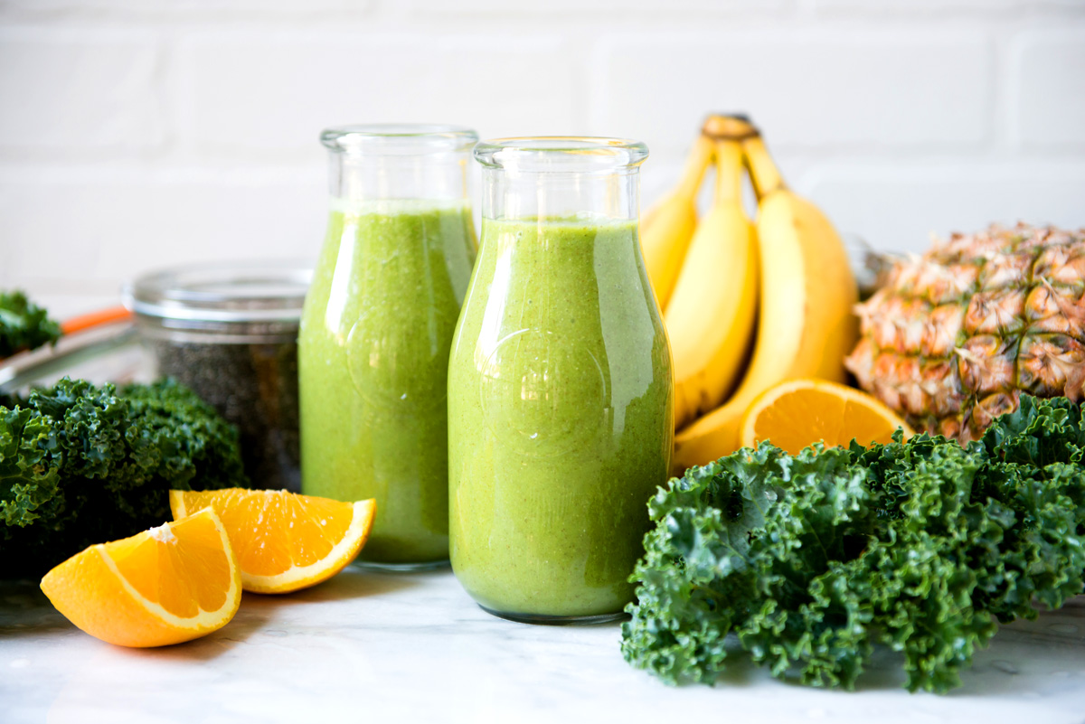 Fresh oranges, kale and banana next to a coconut water smoothie.
