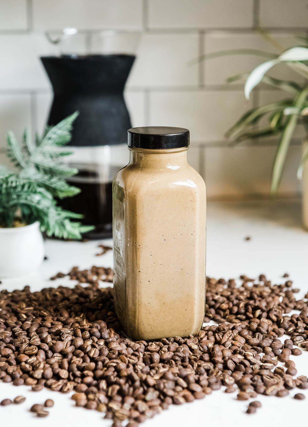 mocha smoothie in a glass container with a black lid sitting in the middle of a pile of whole coffee beans.