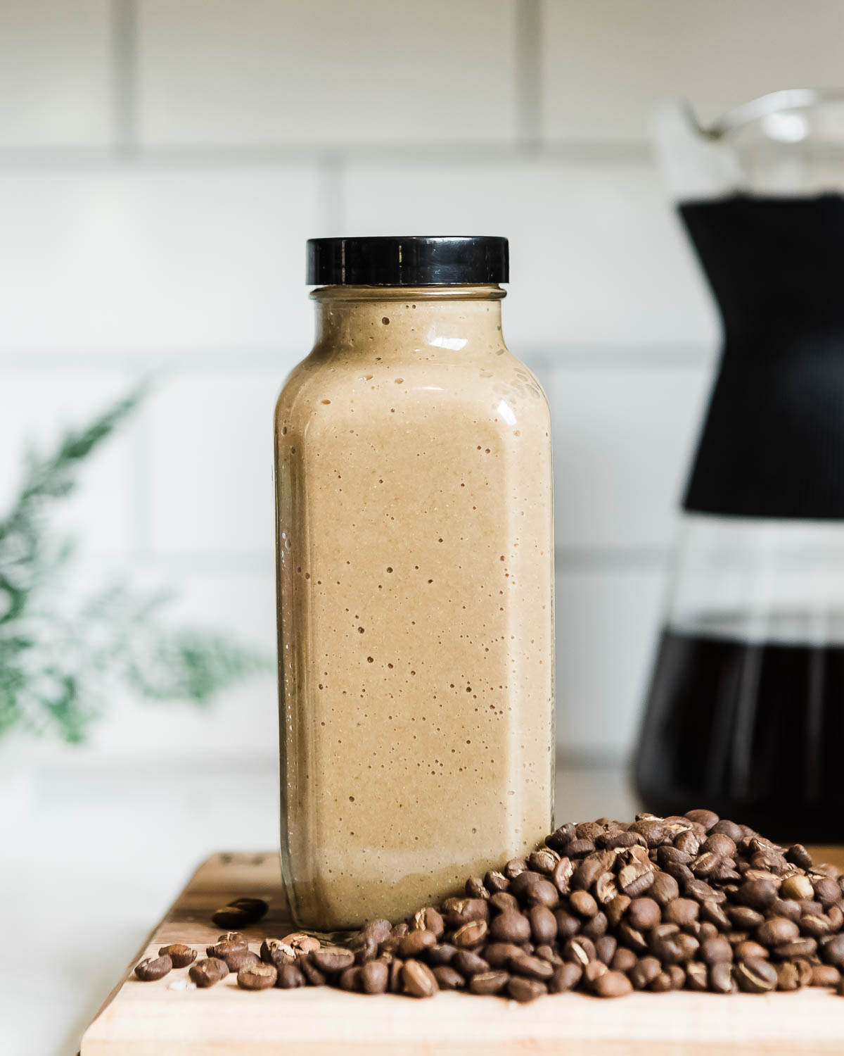 brown colored smoothie in a glass jar with a black lid sitting on a pile of whole coffee beans.
