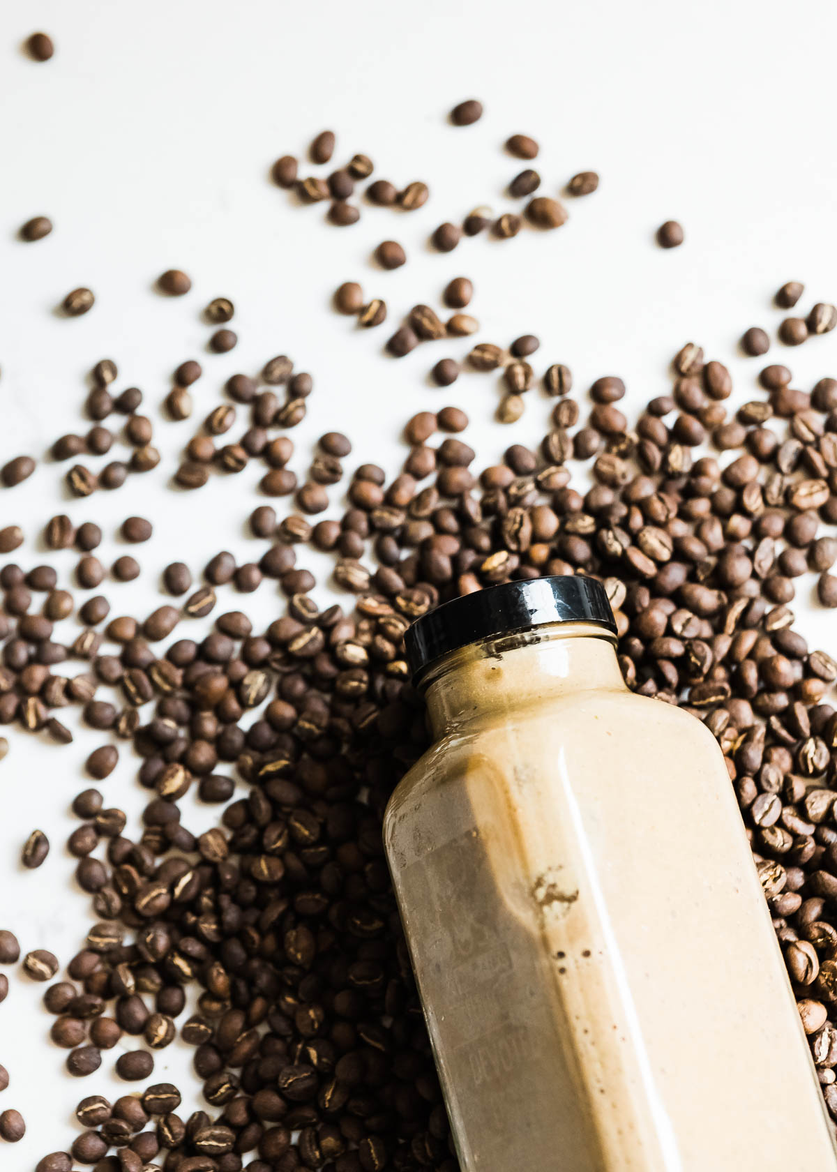 mocha smoothie in a glass container with a black lid lying on a bed of whole coffee beans.