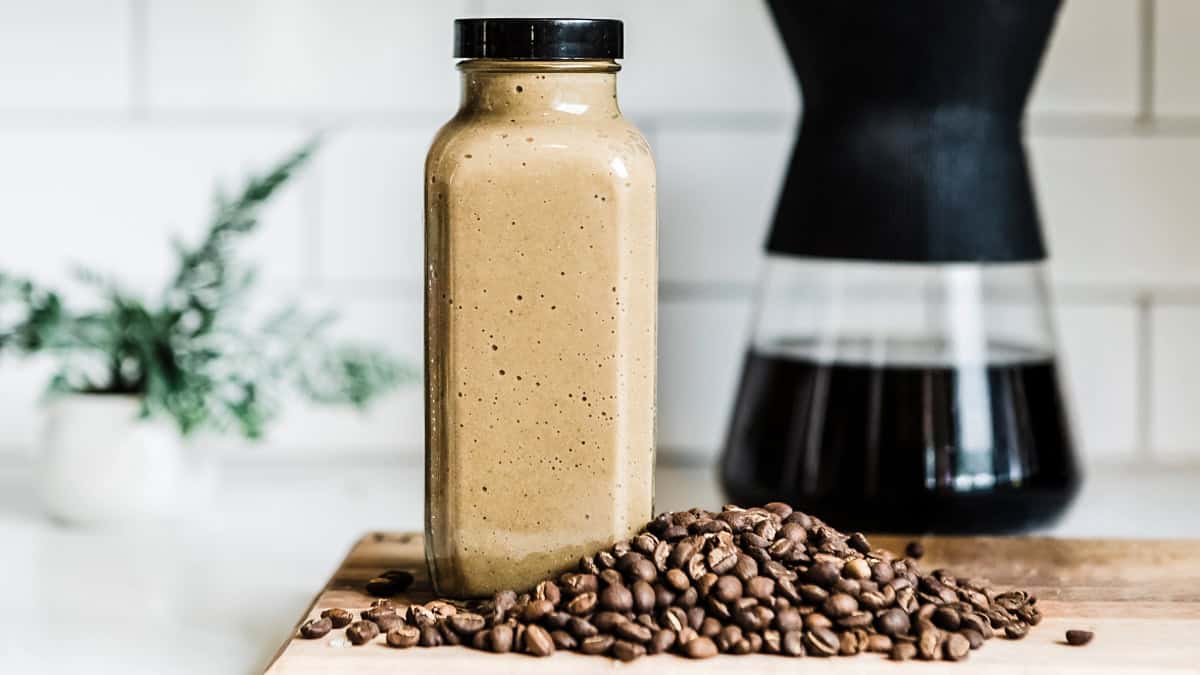 Creamy mocha coffee smoothie in a glass jar with coffee beans nearby.