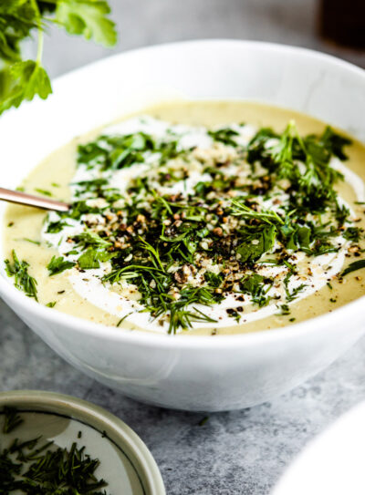 White bowl of celery soup on a table with bunch of fresh parsley.