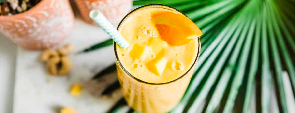 orange colored smoothie on a palm branch with a striped straw in the cup