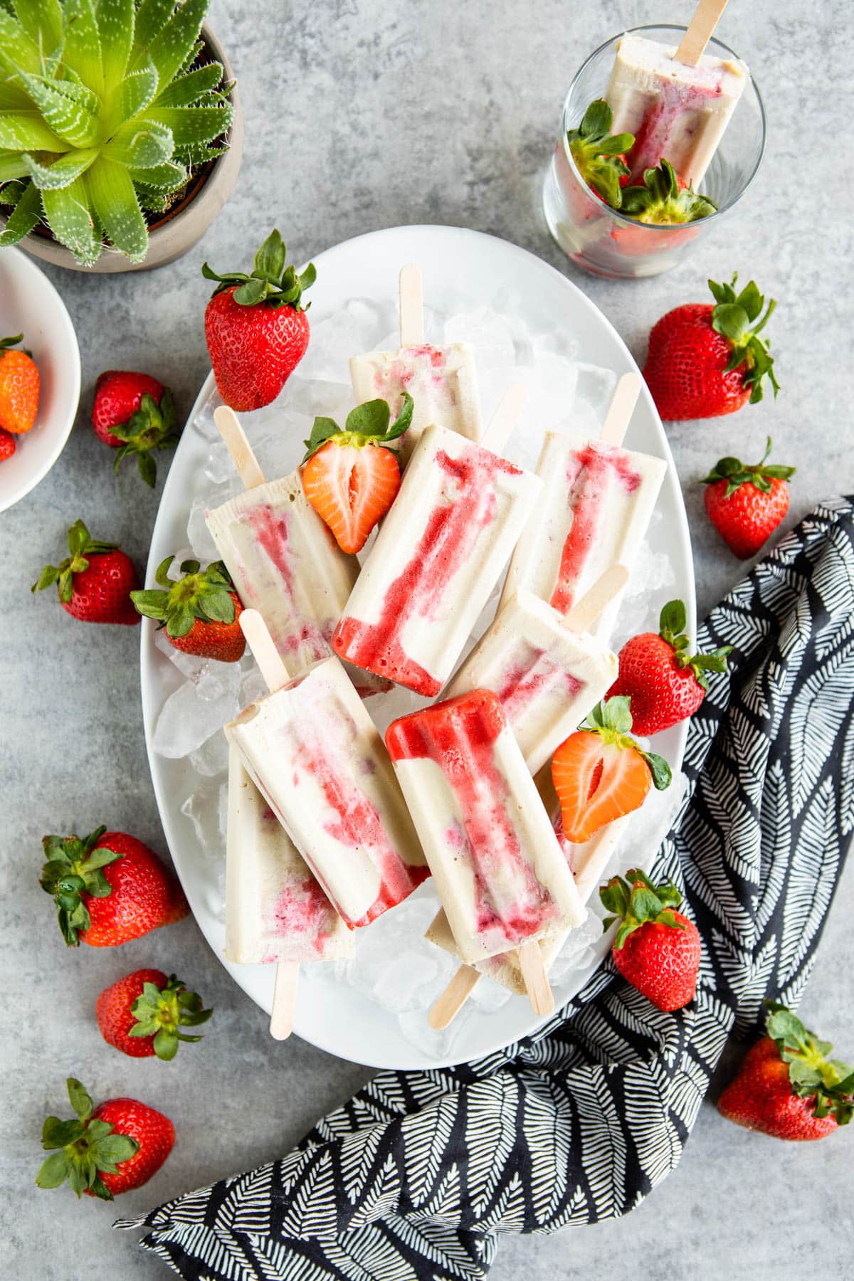 a plate of strawberry popsicles sitting on a pile of ice surrounded by fresh strawberries.